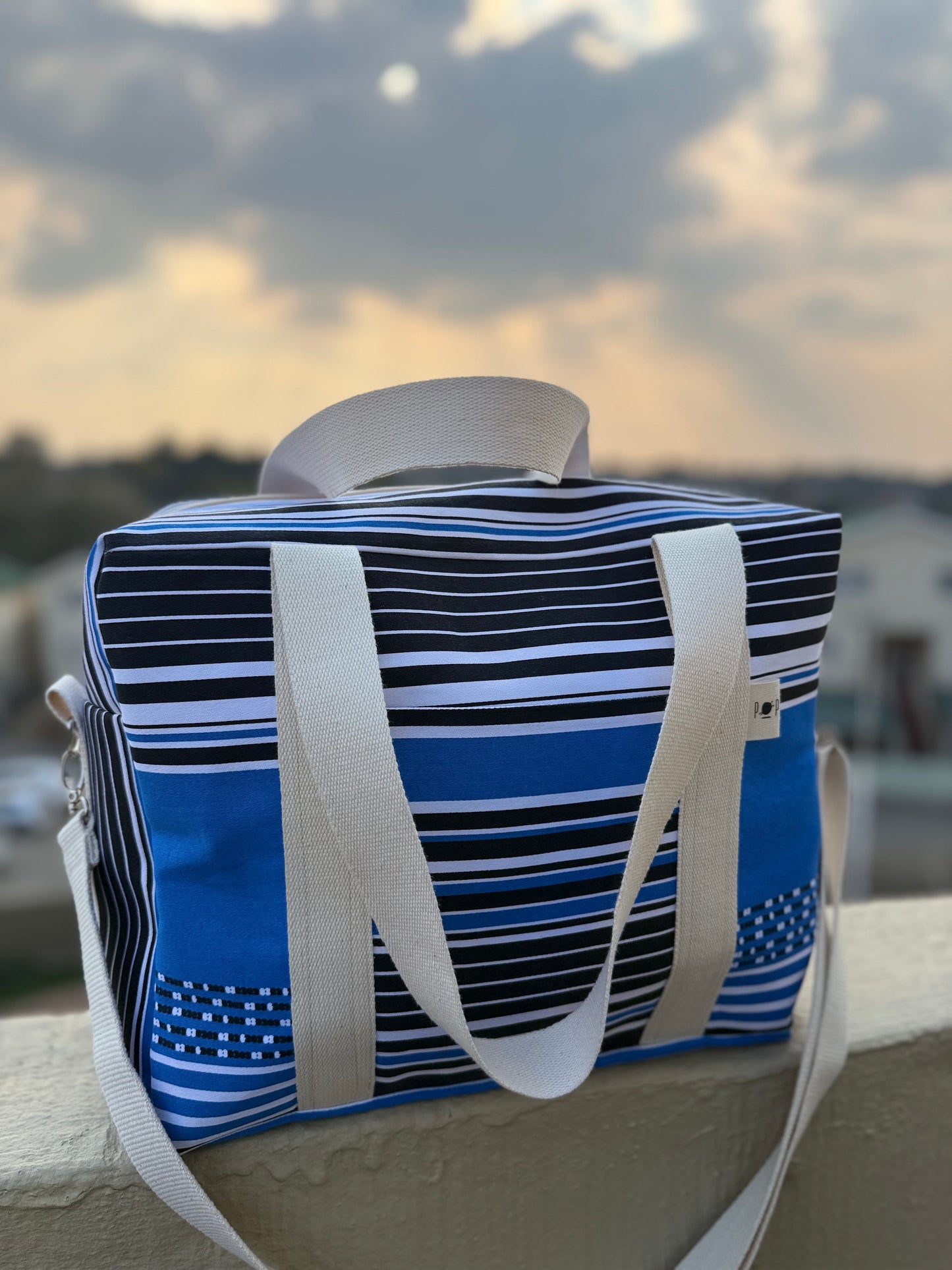 Blue and black striped bag with white straps against a blurred outdoor background