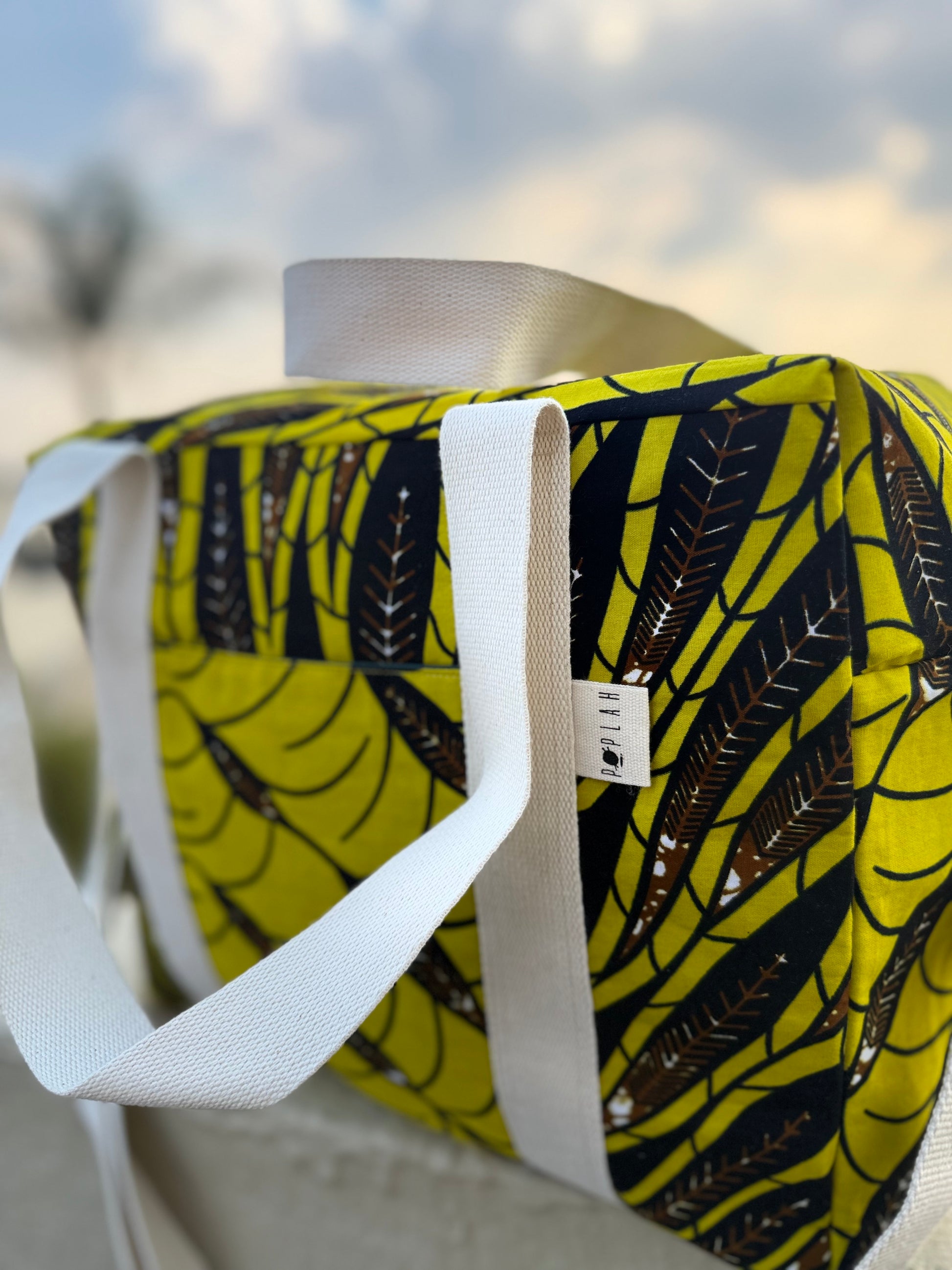 Mustard and brown patterned bag with a white strap on a blurred outdoor background