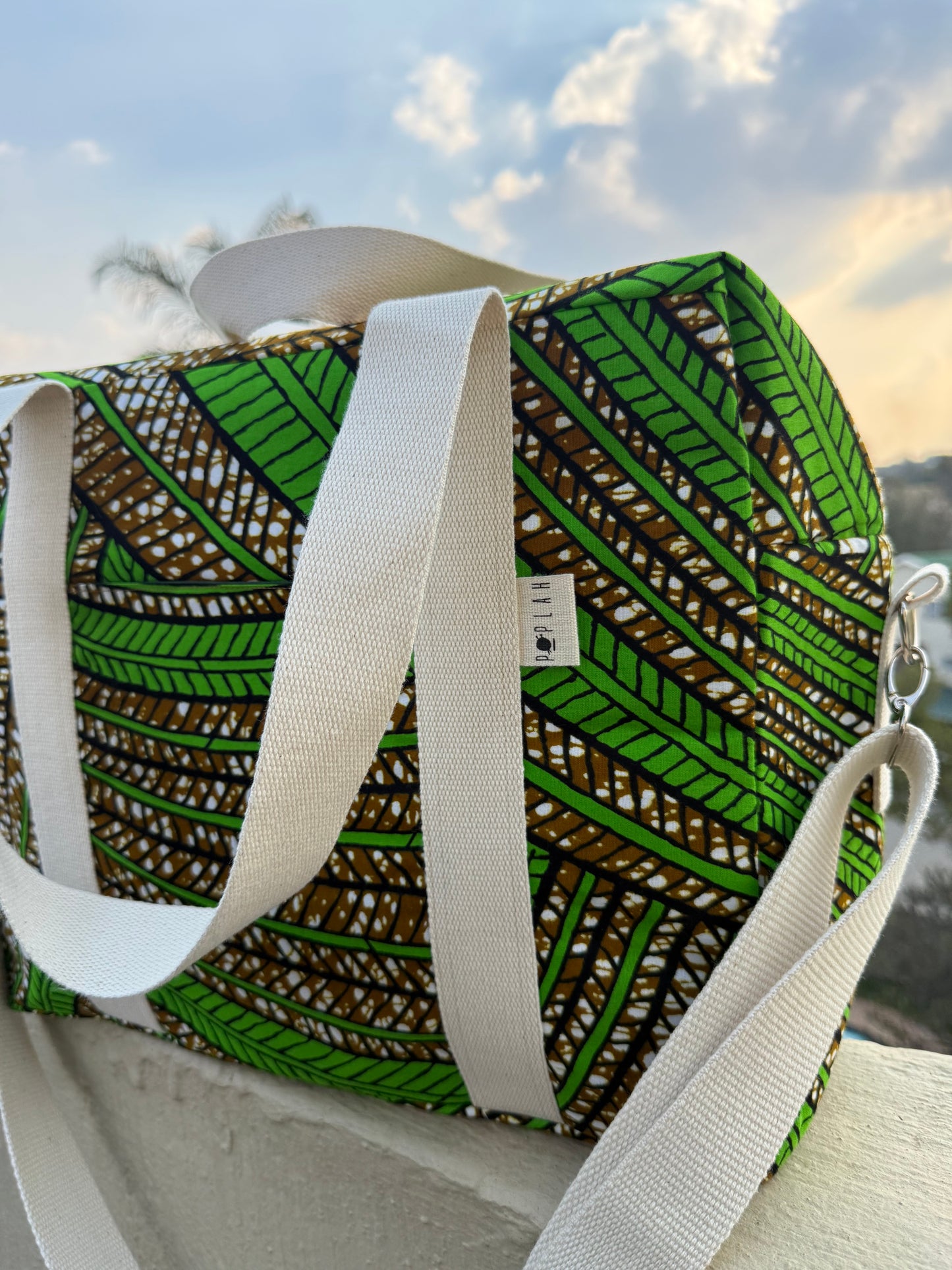 Green and brown patterned bag with white straps on a surface outdoors