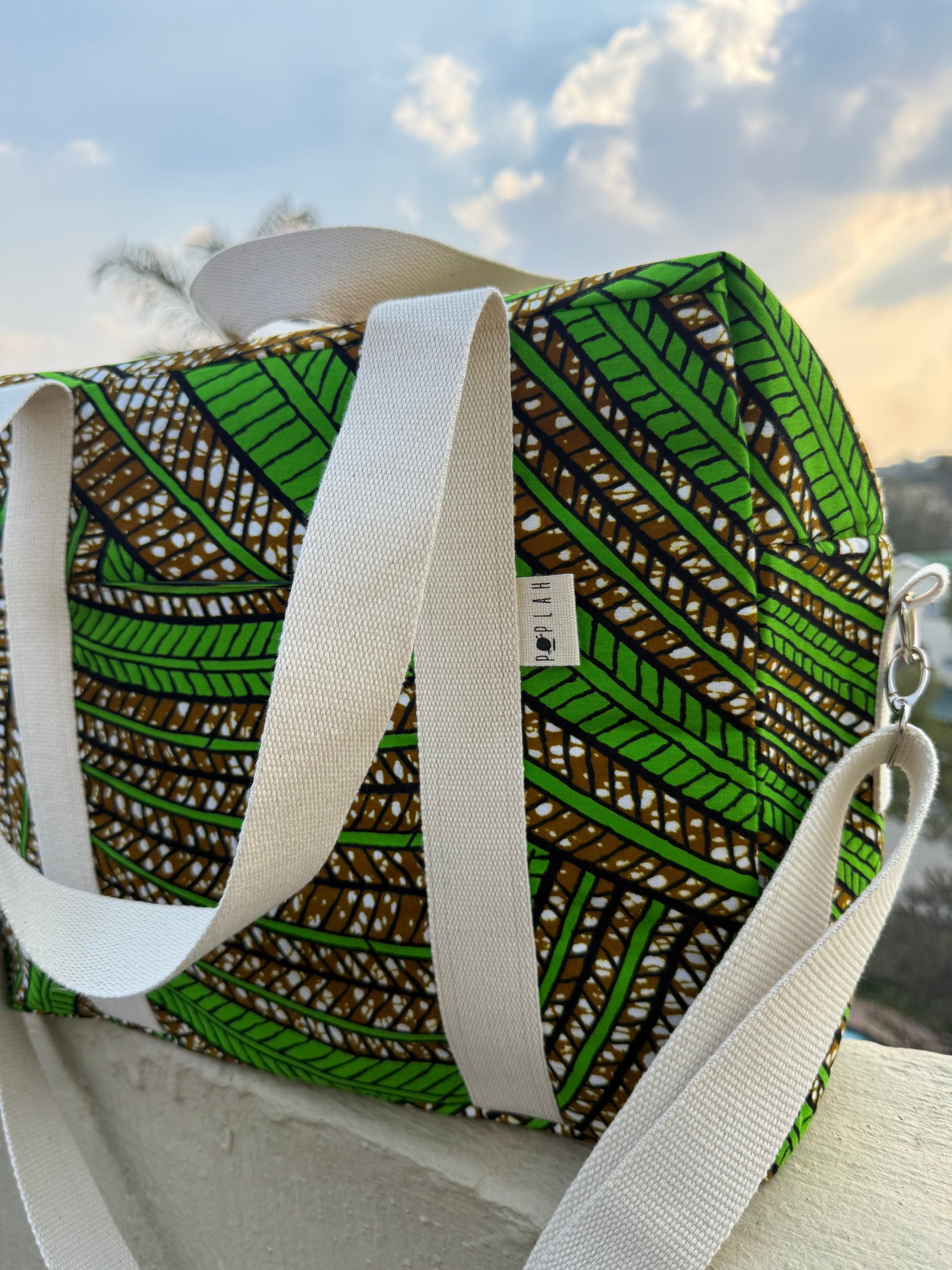 Green and brown patterned bag with white straps on a surface outdoors