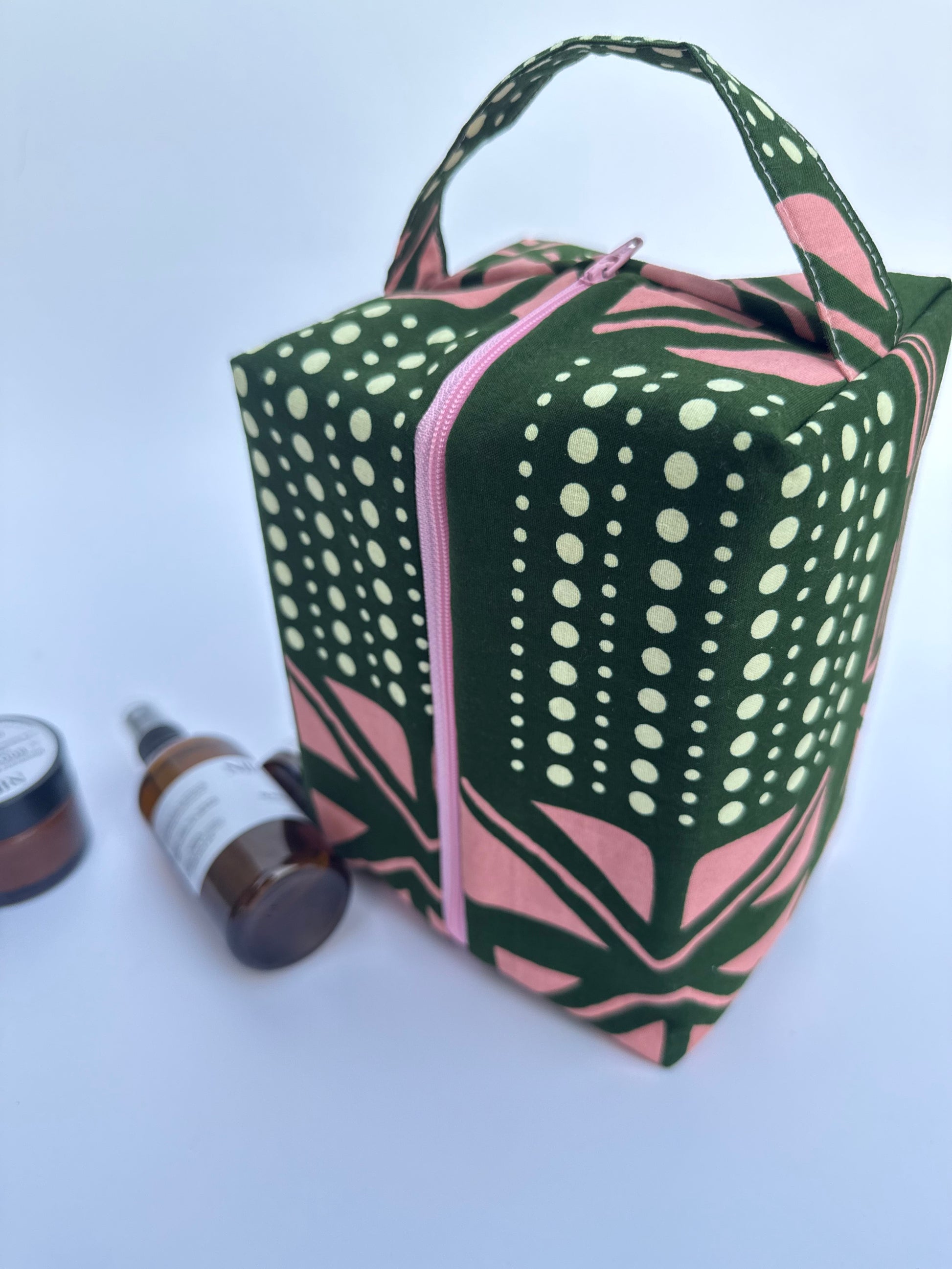 Green and pink patterned toiletry bag with cosmetic items on a light blue background